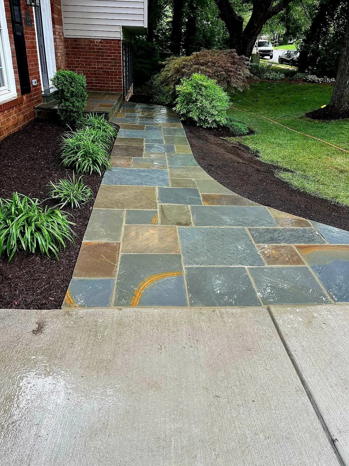 A stone walkway leading to a house with a brick building in the background.