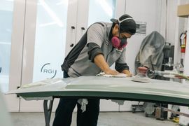 Gloved hand spraying a car door with a paint gun in an auto body shop