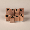 Wooden blocks spelling “FEED BACK” in black letters on a beige background
