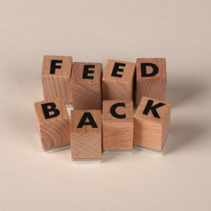 Wooden blocks spelling “FEED BACK” in black letters on a beige background