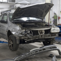 Damaged black sedan in an auto repair shop with hood open and front bumper removed