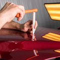 Hand polishing a red car with a cloth and orange applicator pad