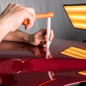 Hand polishing a red car with a cloth and orange applicator pad