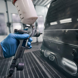 Blue-gloved hand sprays black car door with a paint gun in an auto body shop
