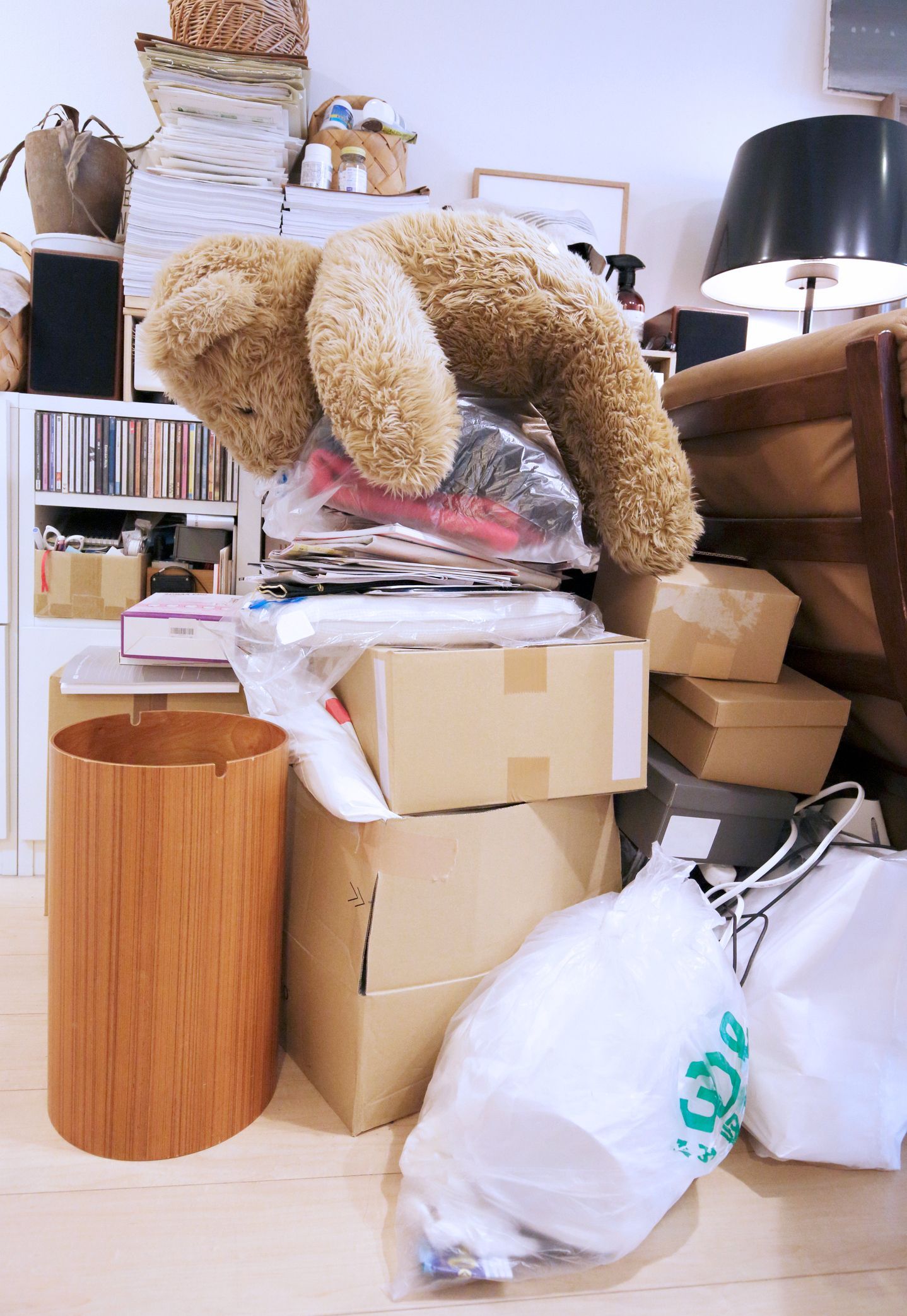 A pile of boxes, bags, and a teddy bear in a cluttered room.
