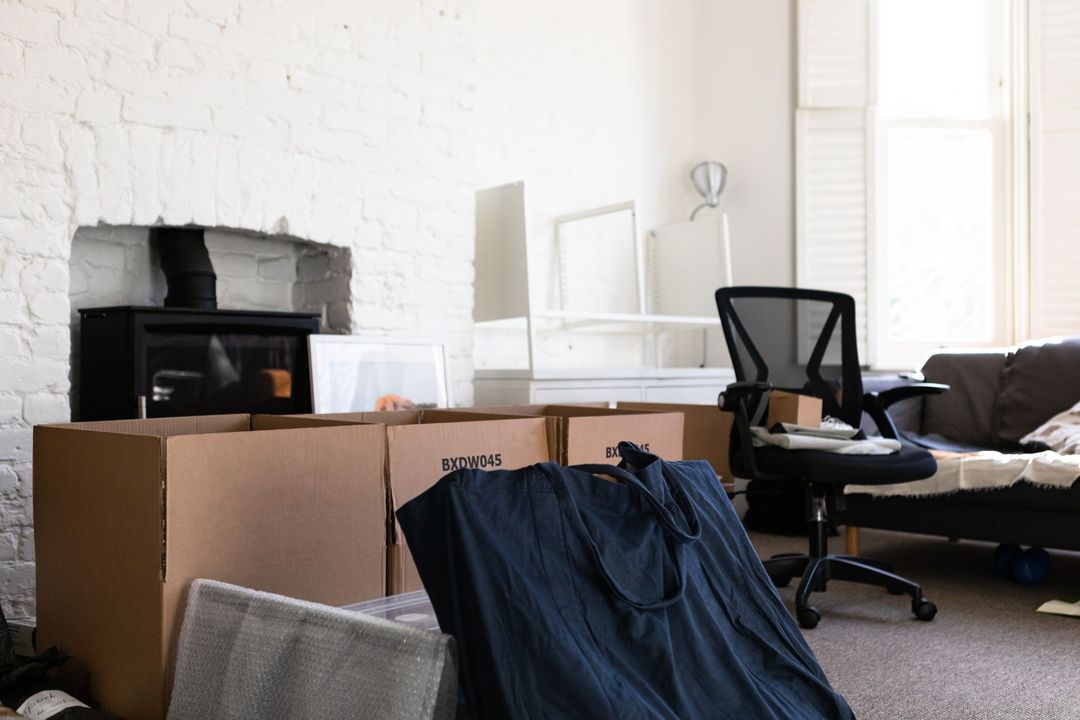 An interior shot showing a room with packed moving boxes, furniture, and a fireplace. A dark chair is in the room.