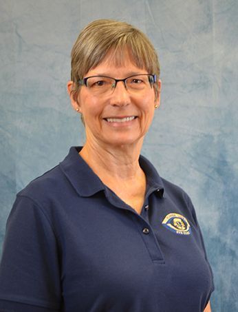 Woman in glasses and navy shirt smiles, against a blue backdrop.