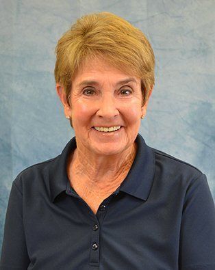 Woman with short blonde hair smiles, wearing a navy blue collared shirt; blue and white background.