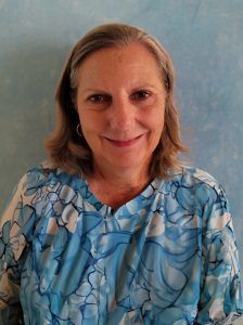 Woman in a blue floral top smiles at the camera, with a light blue background.