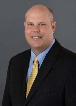 Man in suit and tie smiling against a dark background.