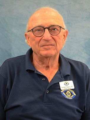 Man wearing glasses and a blue shirt, smiling slightly, with a name tag.