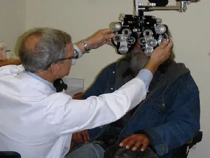 Optometrist examining a patient's eyes with a phoropter in an office.