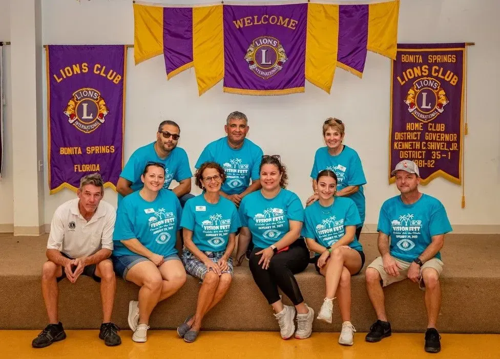 Group of people in matching blue shirts pose in front of Lions Club banners.