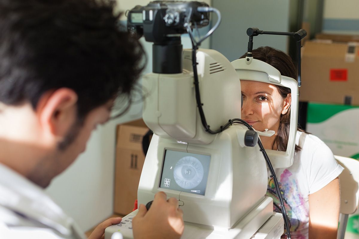 Optometrist examining a patient's eye with an autorefractor device in a clinic setting.