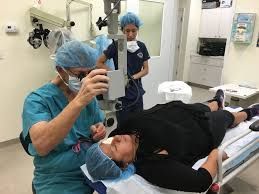 Doctor examining a patient's eye with a microscope during an eye surgery in a medical setting. An assistant is present.