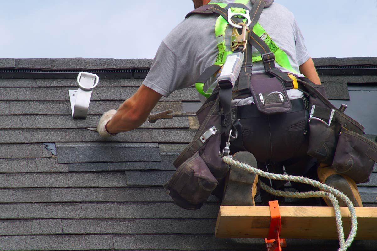 A man wearing a safety harness is working on a roof