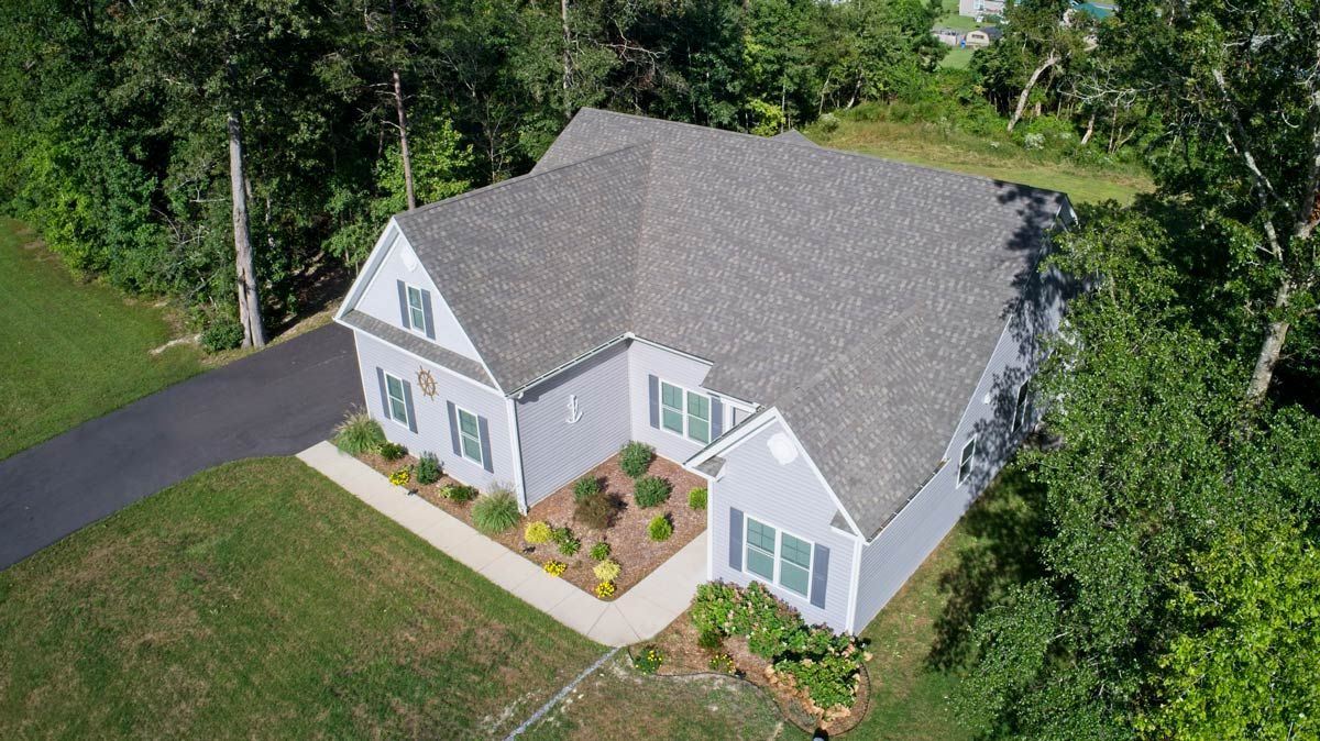 An aerial view of a white house with a gray roof surrounded by trees