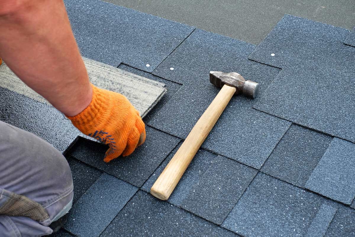 A man is installing shingles on a roof with a hammer