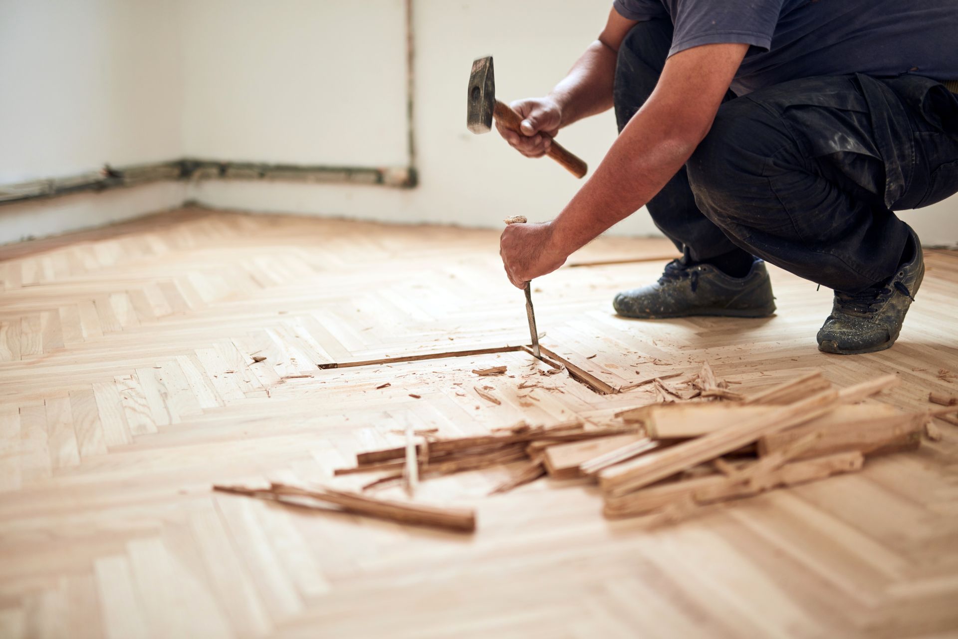 Man removing wood flooring with a hammer and chisel.
