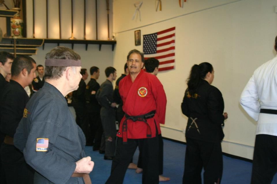 A man in a red karate uniform stands in front of an american flag