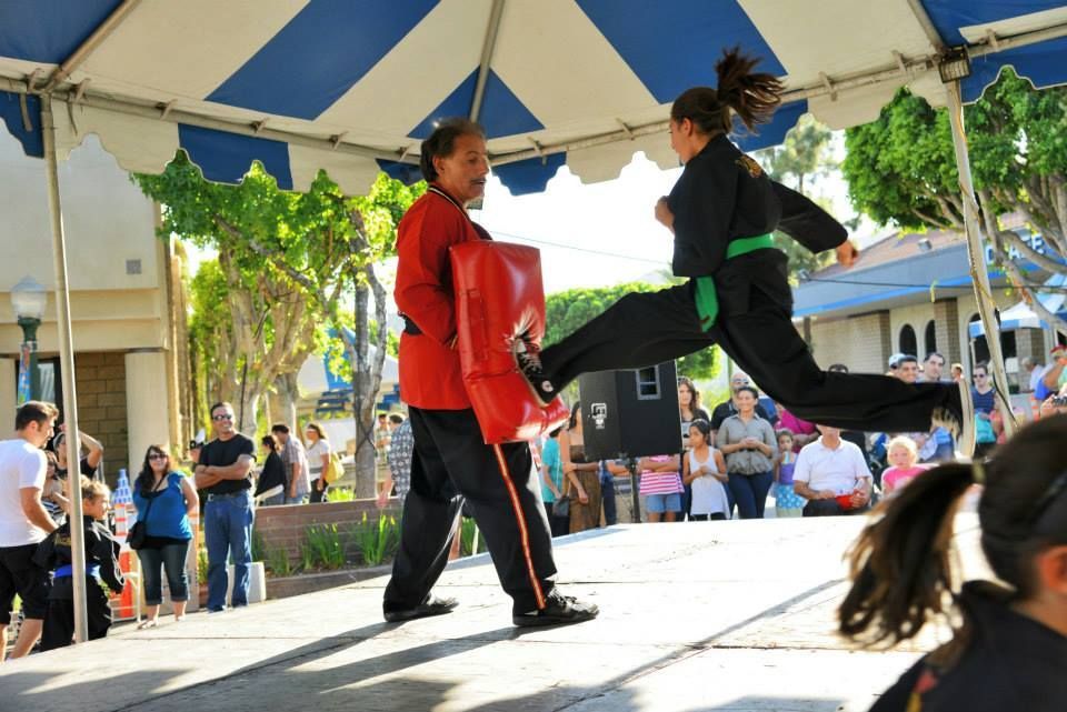 A man in a red jacket is standing next to a woman in a green belt who is kicking in the air