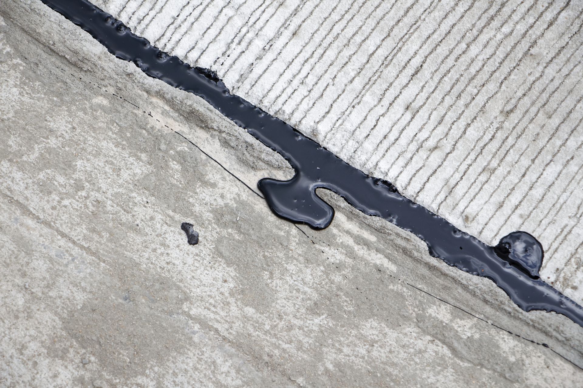 Black sealant along a crack in a concrete surface.