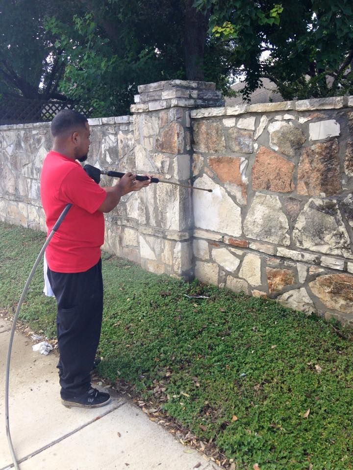 Person in red shirt power washing a stone wall.
