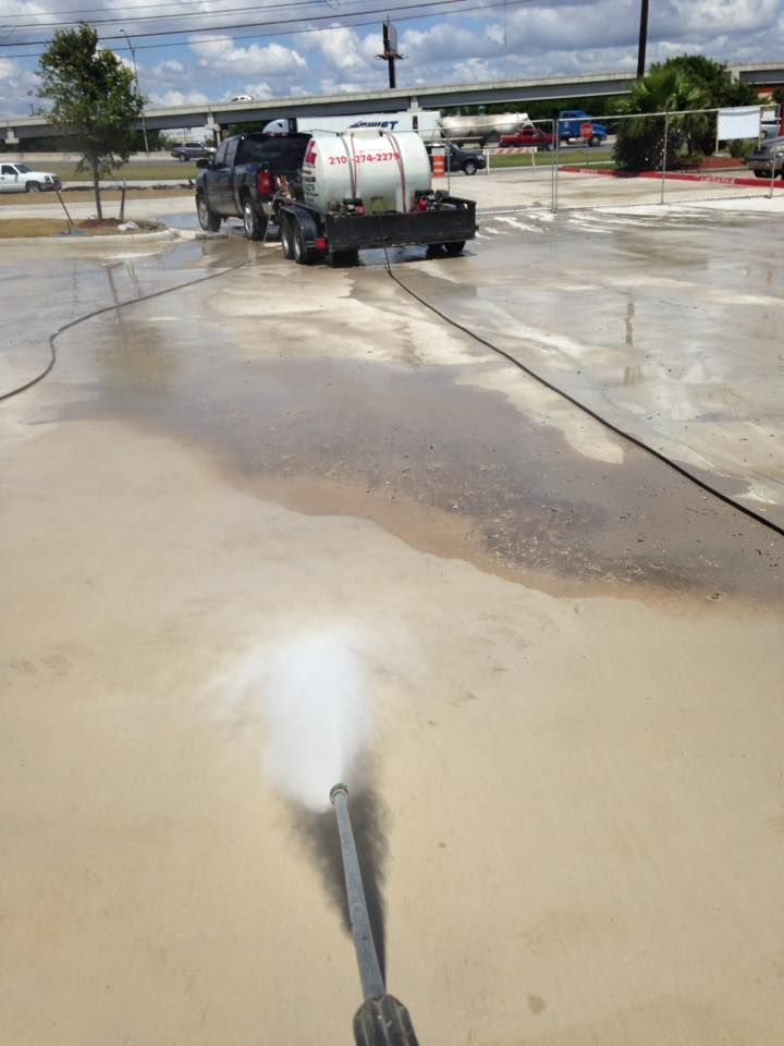 A person is using a high pressure washer to clean a parking lot.