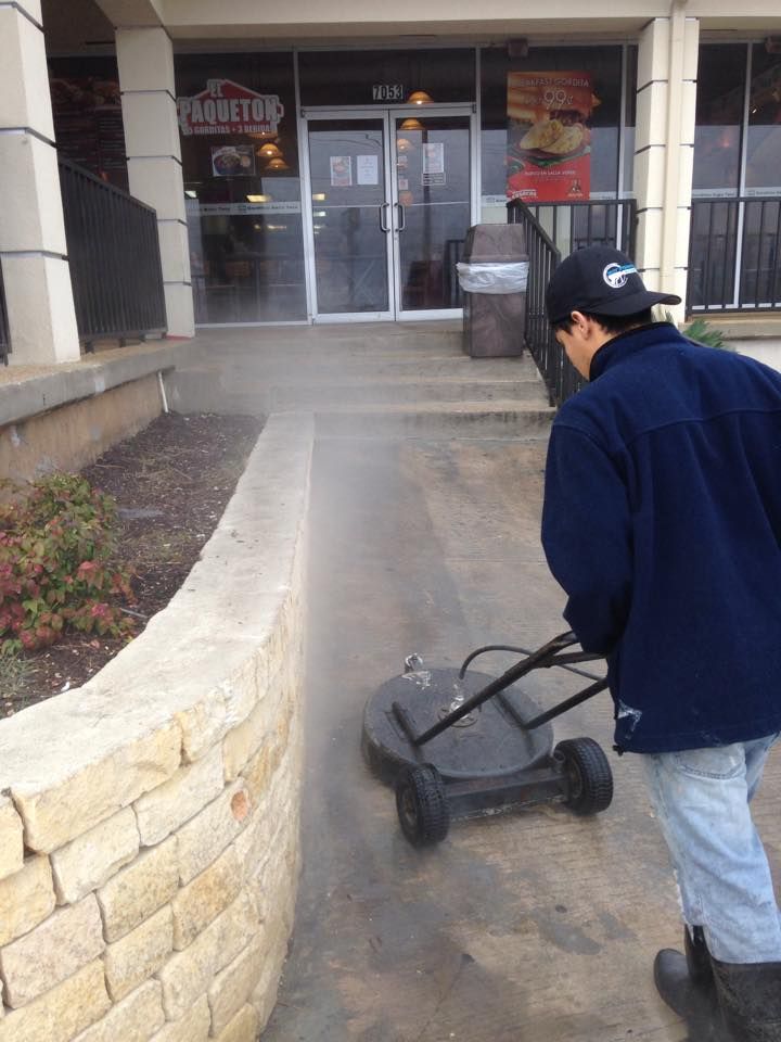A man is using a machine to clean the sidewalk in front of a restaurant.