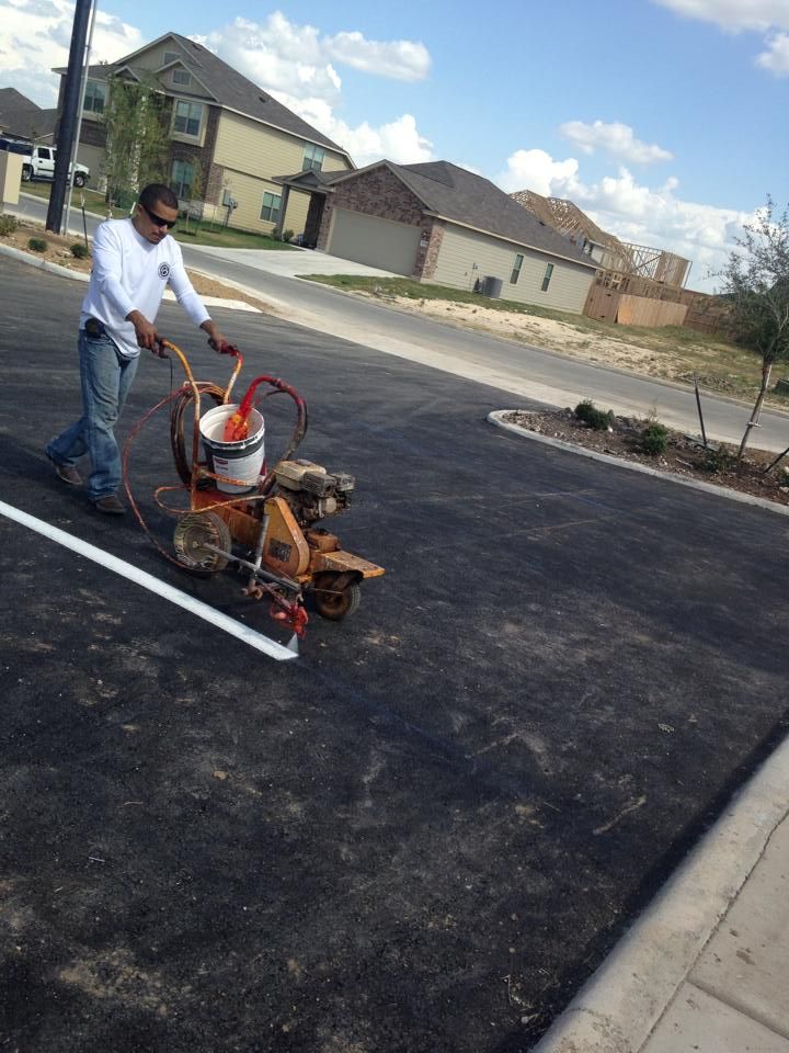 A man is using a machine to paint a white line on a parking lot.
