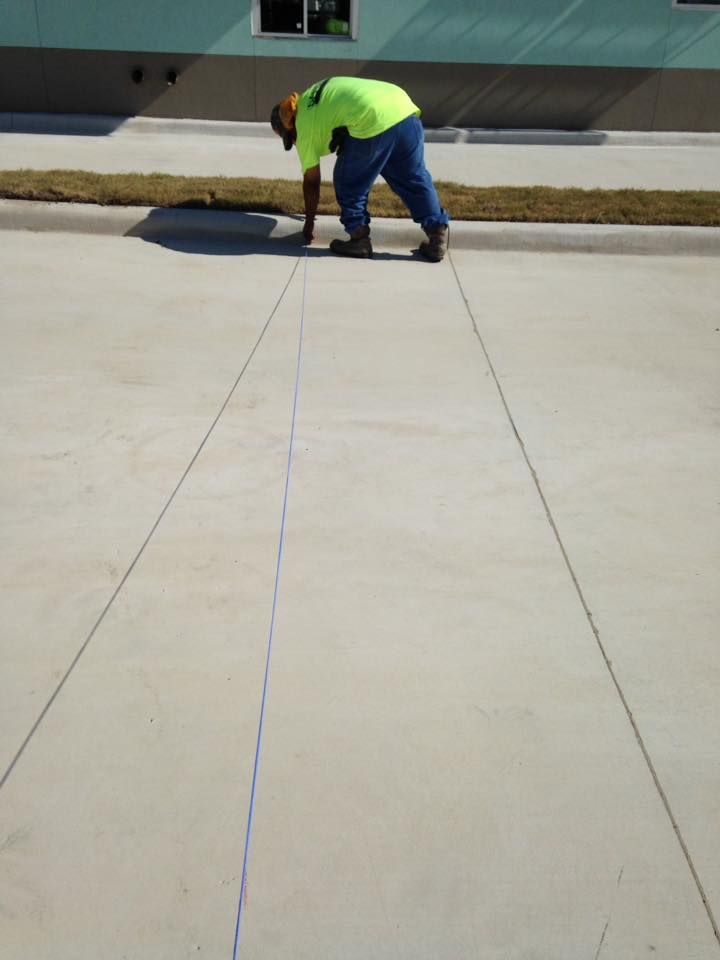 A man in a neon yellow shirt is measuring a line on a concrete surface