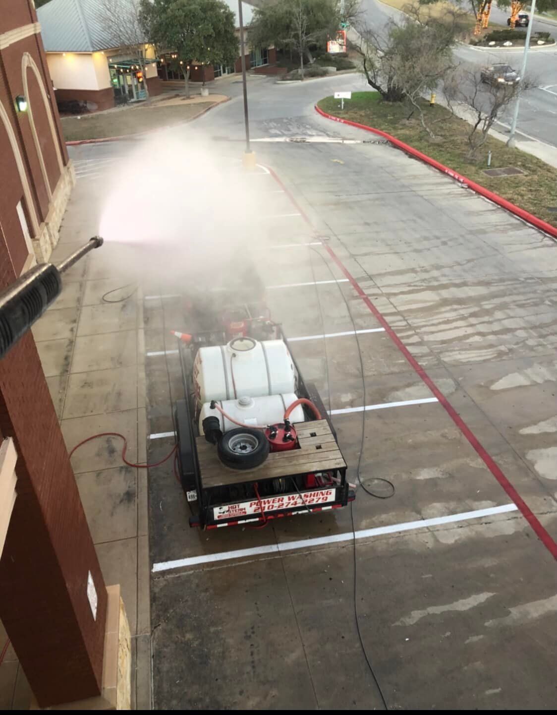 A worker pressure washes a parking space. A trailer with water tanks is behind the building.