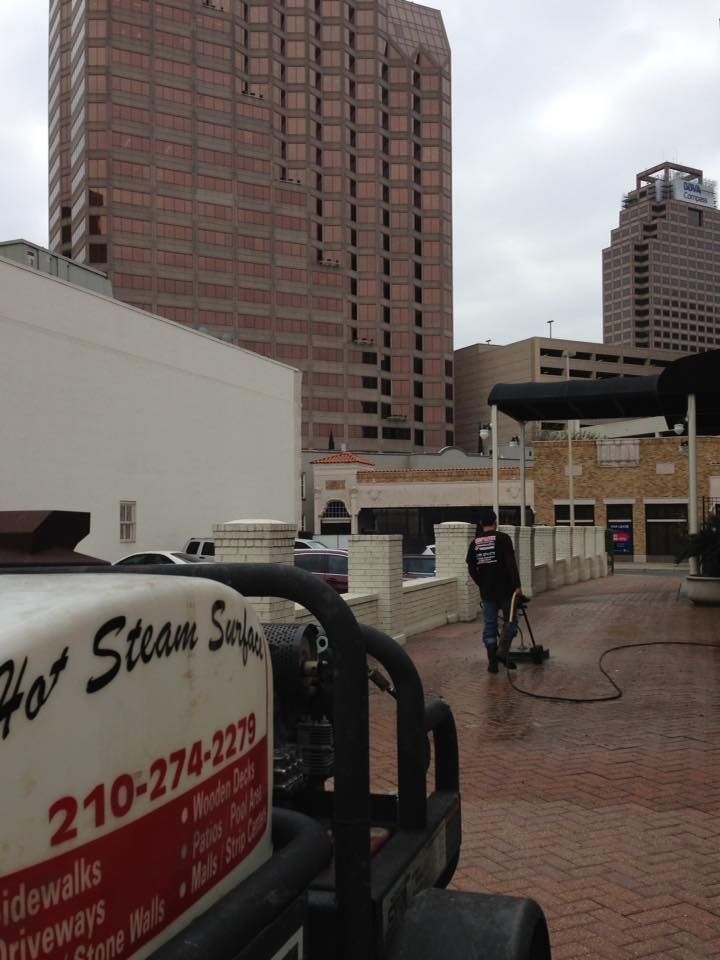 A man is cleaning a sidewalk with a steam cleaner