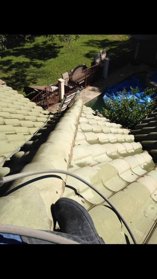 A person is standing on the roof of a house with a pool in the background.