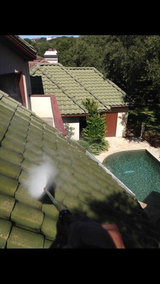 A person is cleaning the roof of a house with a pressure washer.