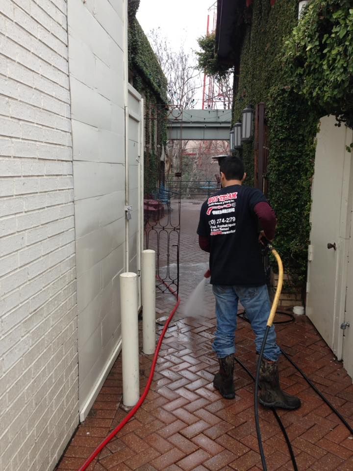 A man is cleaning a brick sidewalk with a hose.
