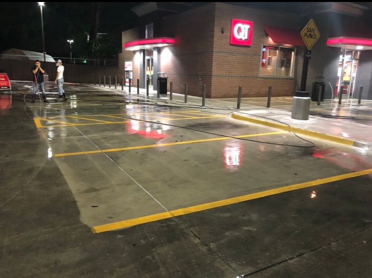 QT gas station exterior with wet pavement and yellow parking lines. People near entrance.