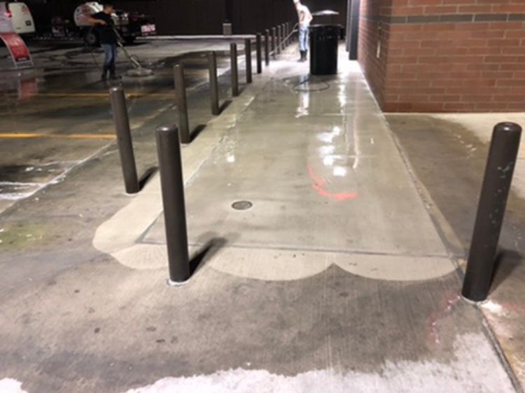 Wet concrete sidewalk with bollards in front of a building.