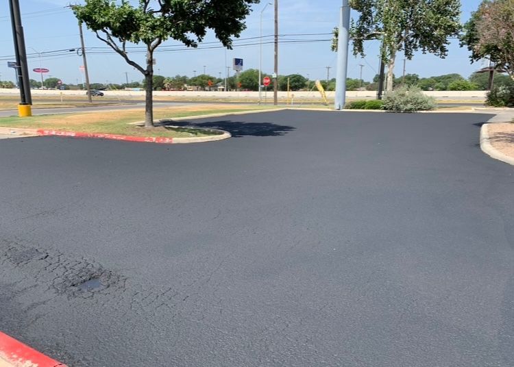 Newly paved asphalt parking lot with trees and curbs in the background.