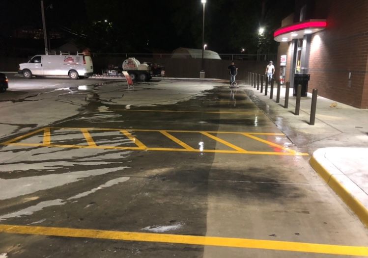 Wet parking lot at night with yellow parking space lines. A van and people are visible.