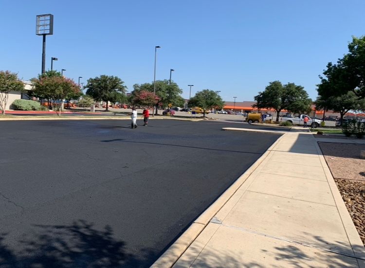 Workers applying sealant to a freshly paved parking lot on a sunny day.