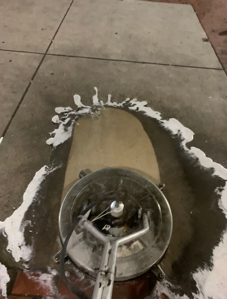 Sidewalk being cleaned with a rotating surface cleaner, creating a soapy trail.