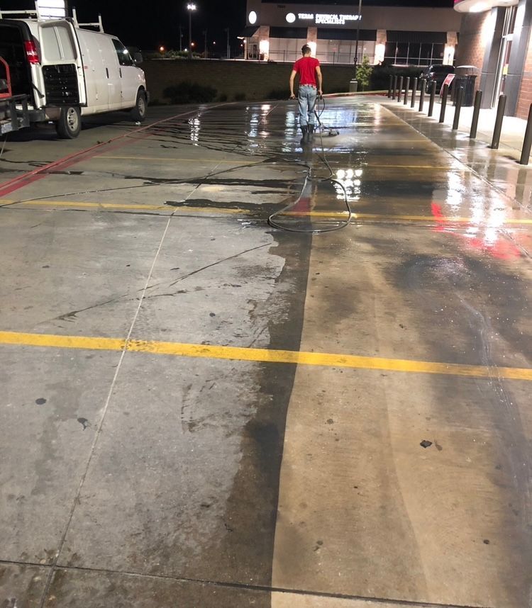 Person power washing a concrete parking lot at night.