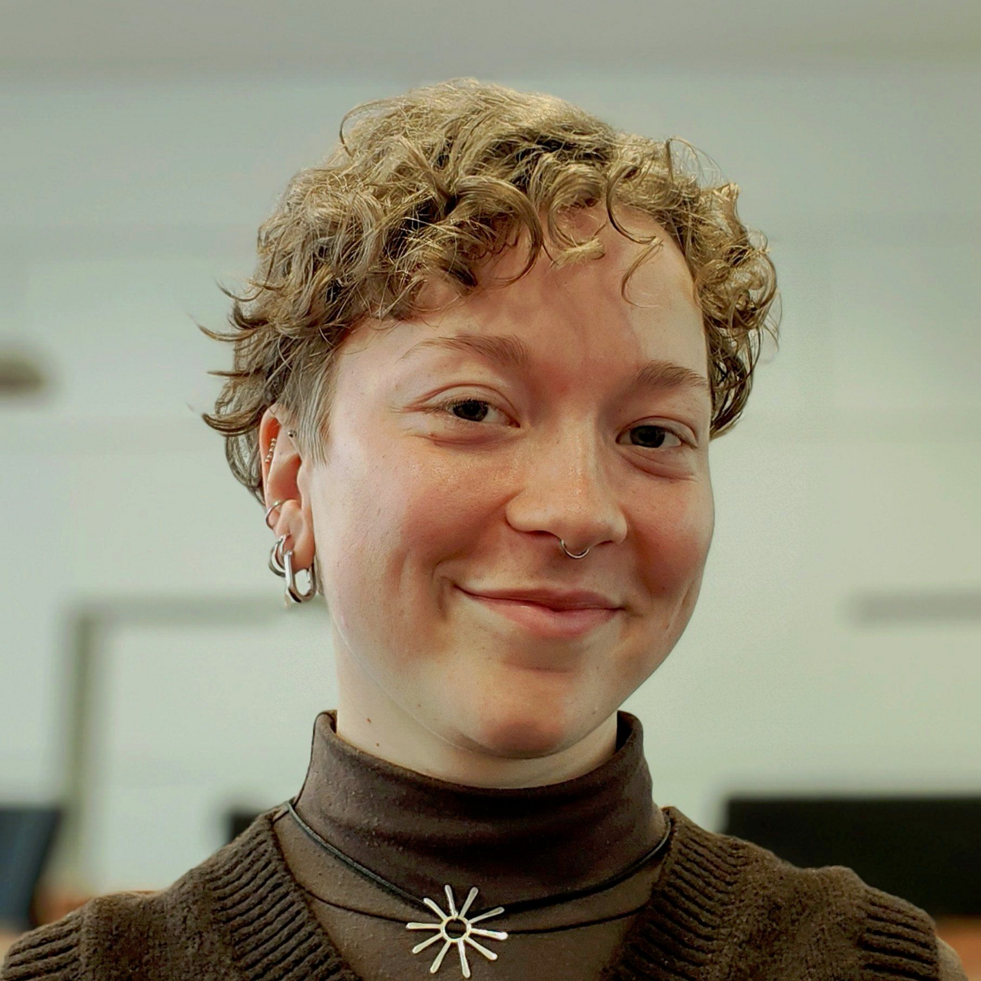 Woman with short blonde hair smiles, wearing an orange patterned shirt, in front of a Heineken sign.