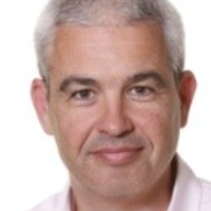 Man with gray hair, smiling, in a light-colored shirt. Portrait against a white background.