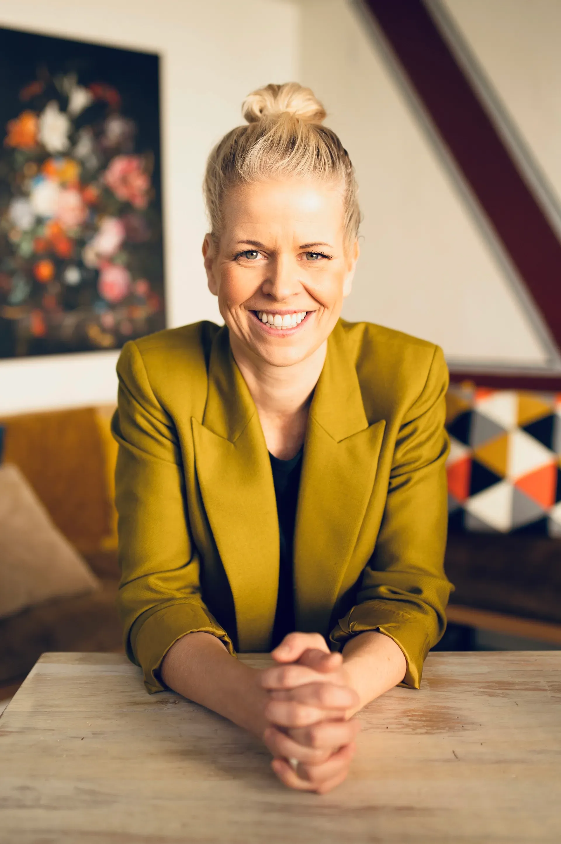 Woman in green shirt smiles outdoors, head tilted, hand to her face.
