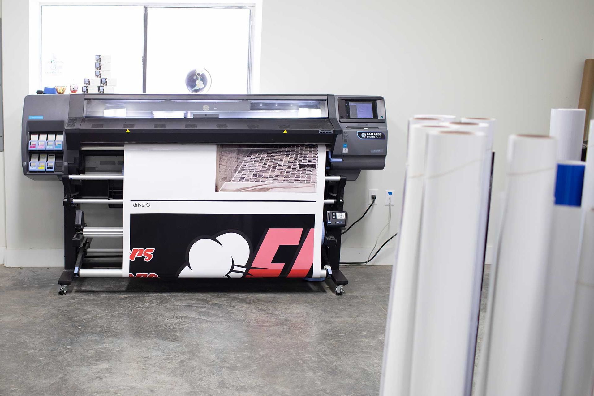 Wide-format printer producing a large black and white graphic; rolls of white paper in the foreground.
