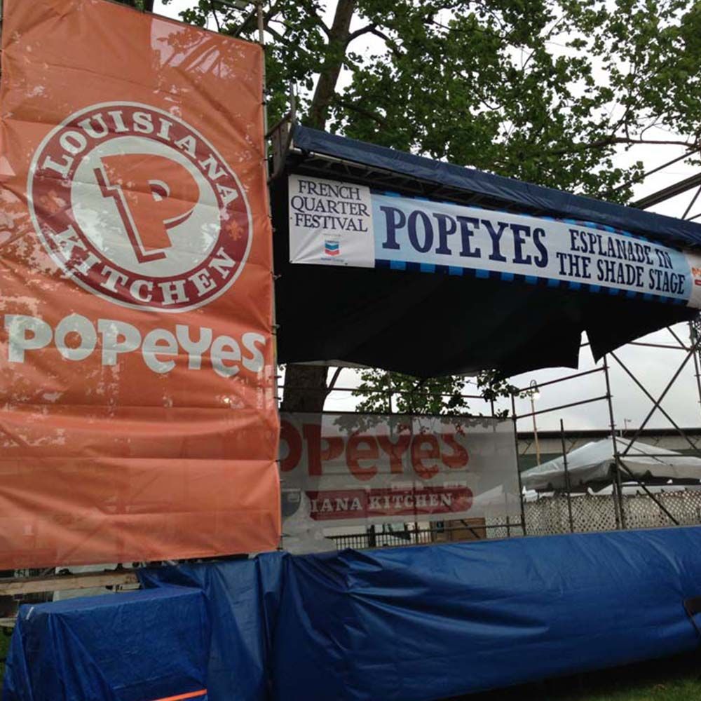 Popeyes Louisiana Kitchen food stand at the French Quarter Festival, with orange and blue signage, outdoors.
