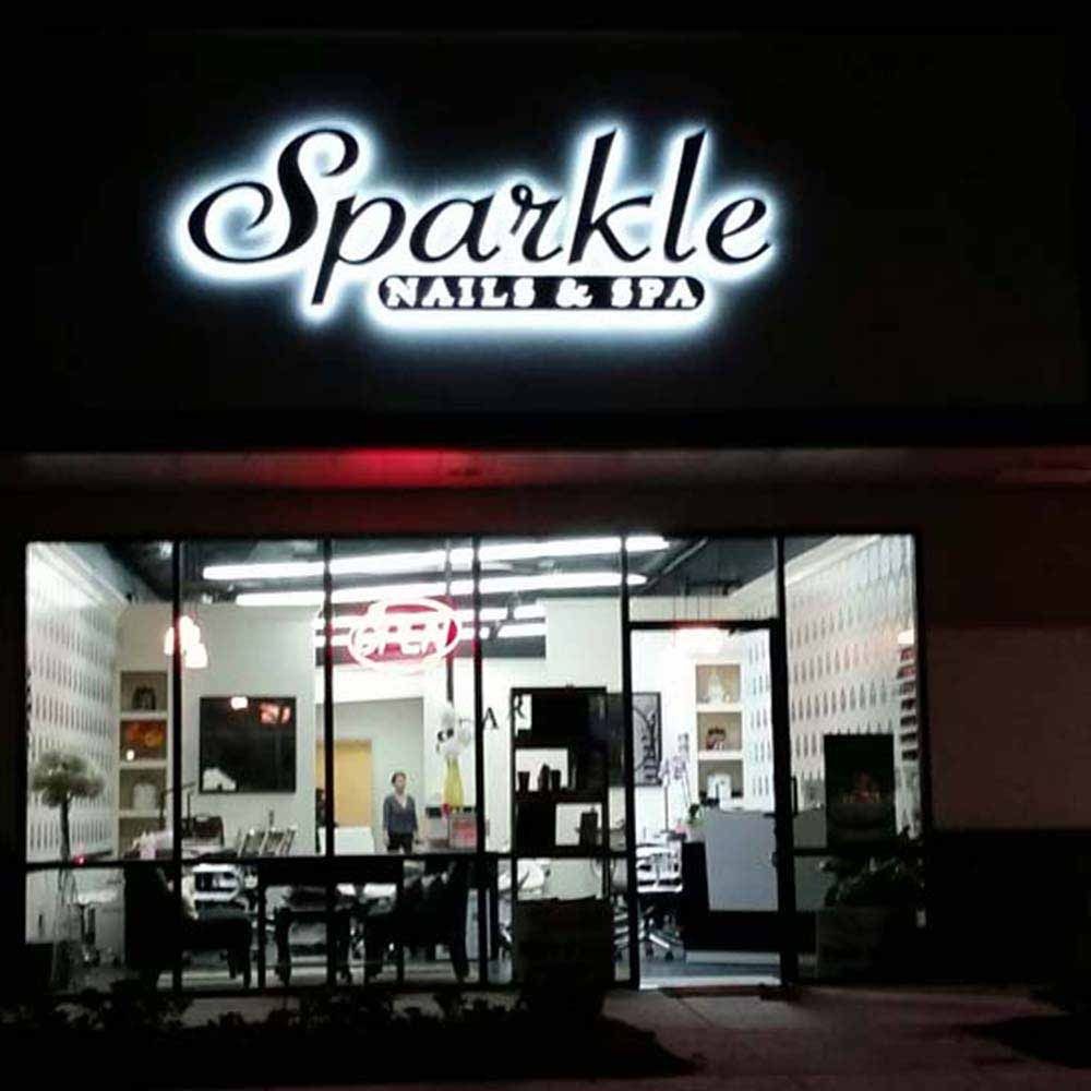 Sparkle Nails & Spa storefront at night, illuminated sign above glass windows, view of interior.