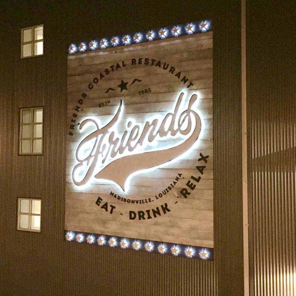 Friends Coastal Restaurant sign on wooden background; illuminated